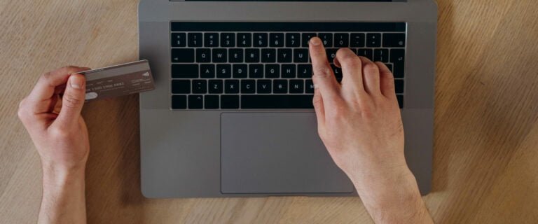 Someone holding a card and typing payment details into a laptop