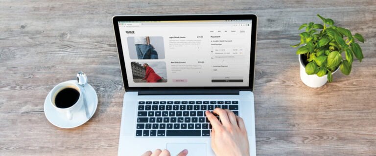 E-commerce website on a laptop surrounded by a coffee and a plant on the desk