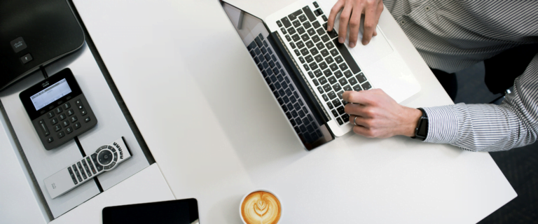 Birdseye view of a man working on laptop on a white desk