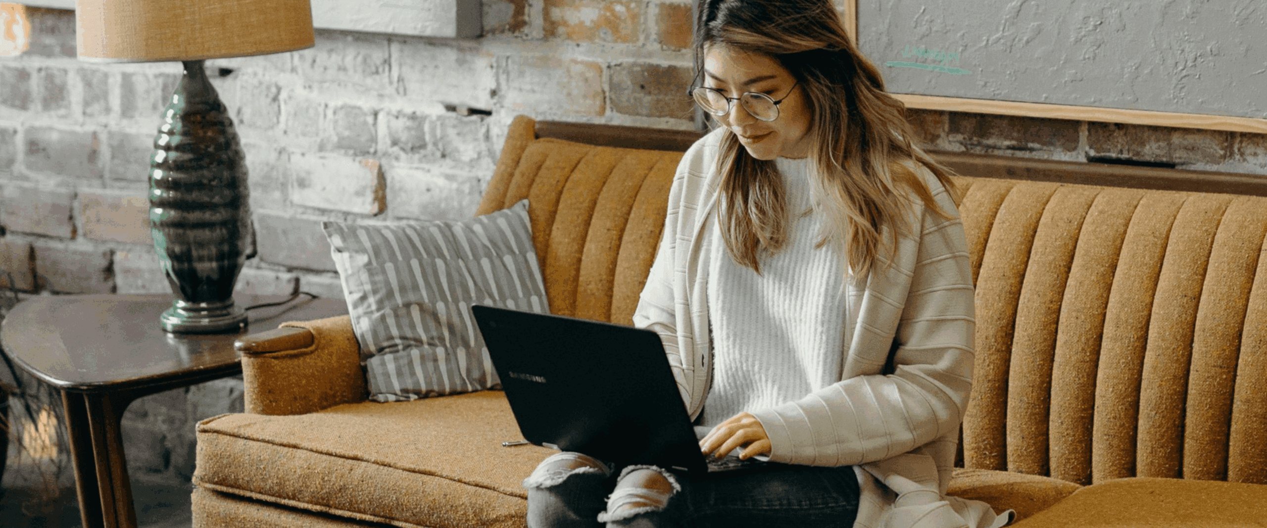 A woman sat on a sofa with a laptop on her knee