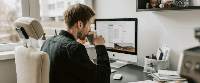 Man sipping a cup of tea while sat at his desk, working on his computer